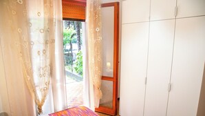 A room with a bed, a wardrobe, and a door leading to an outdoor area with a view of greenery. - Pinewood Escape With Garden (Eraclea)