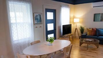 Un salon moderne comprenant un coin repas, un plancher en bois, un téléviseur à écran plat, un canapé et une lampe.