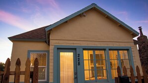 Une maison de plain-pied avec une porte et des fenêtres bleues, une clôture en bois et une cheminée en pierre.