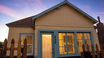 Une maison de plain-pied avec une porte et des fenêtres bleues, une clôture en bois et une cheminée en pierre.