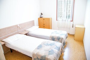 A hotel room with two single beds, a wooden wardrobe, a small desk, and a window with a curtain. - Two Bedroom Flat Close to the Beach in Eraclea (Eraclea)