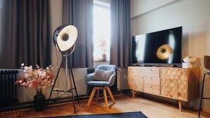 Un salon moderne avec un grand téléviseur à écran plat, un meuble en bois, un tapis bleu et un lampadaire.
