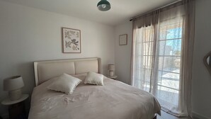 Un dormitori amb llit, dues làmpades de nit, una finestra amb cortines i un quadre a la paret.