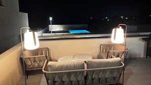 Una terrassa al terrat amb dues cadires de vimetlina i una taula petita, una piscina de fons i una paret de pedra.