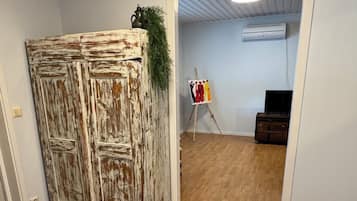 Une pièce avec un plancher en bois, une porte rustique, un petit tableau posé sur un chevalet et un téléviseur.