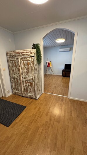 Habitación con suelo de madera, puerta rústica, un pequeño cuadro sobre caballete y un televisor.