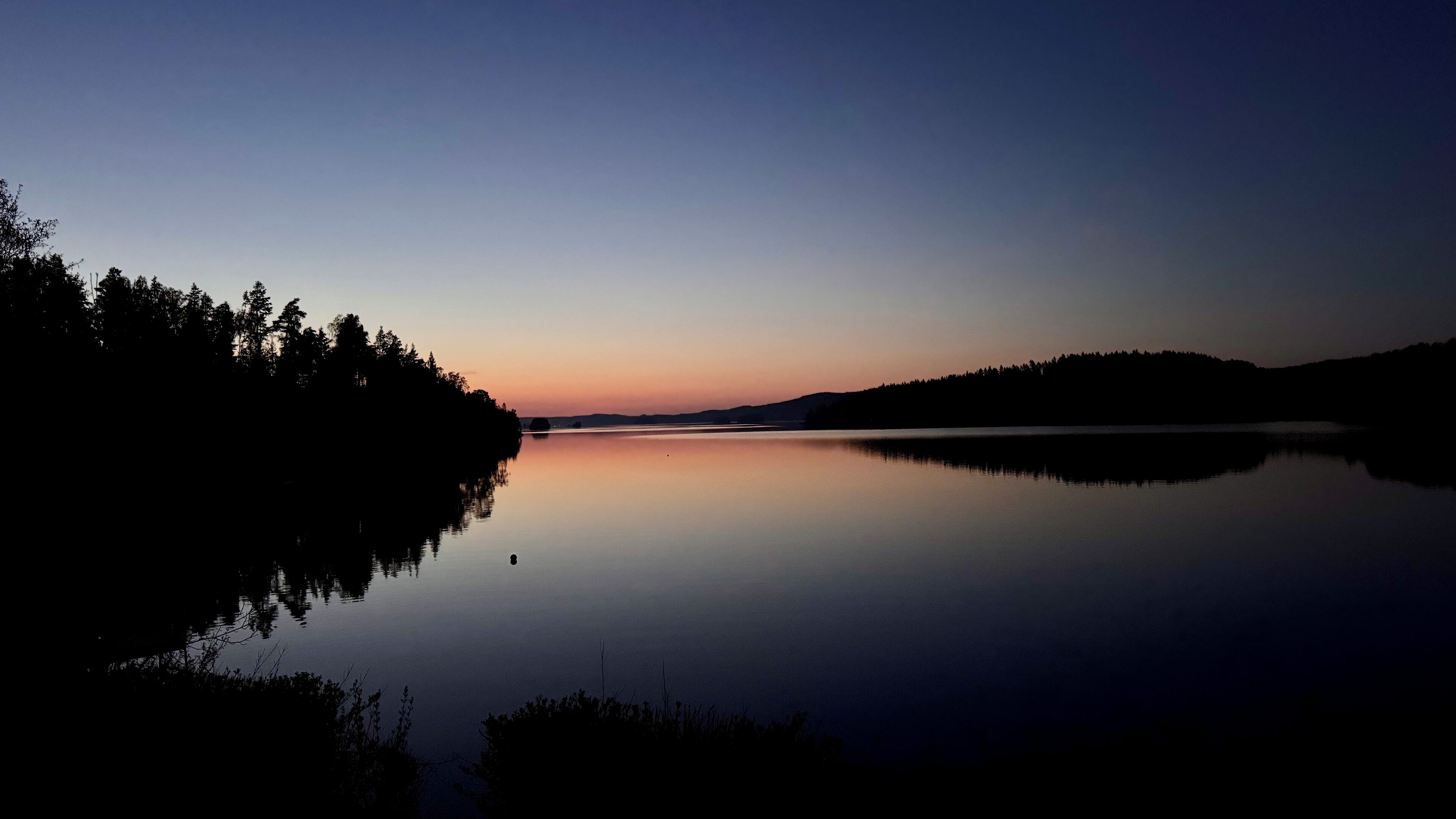 A calm lake at dusk with a forested shoreline.