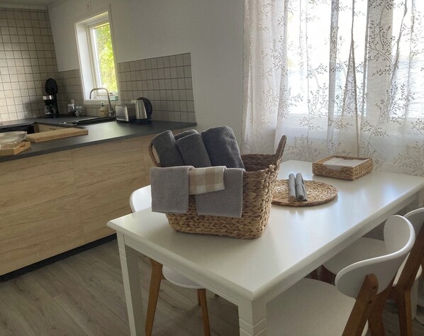 Una cocina moderna con encimera blanca, armarios de madera y un comedor con mesa y sillas blancas.