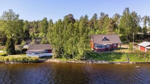 A house by a river with a dock, surrounded by trees and a clear sky.