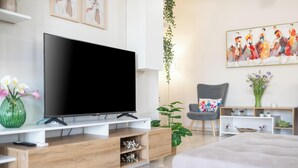 A modern living room with a flat-screen TV, wooden entertainment unit, a grey armchair, and a painting on the wall. - Lumina Apartment with Shared Pool (Perivolia)