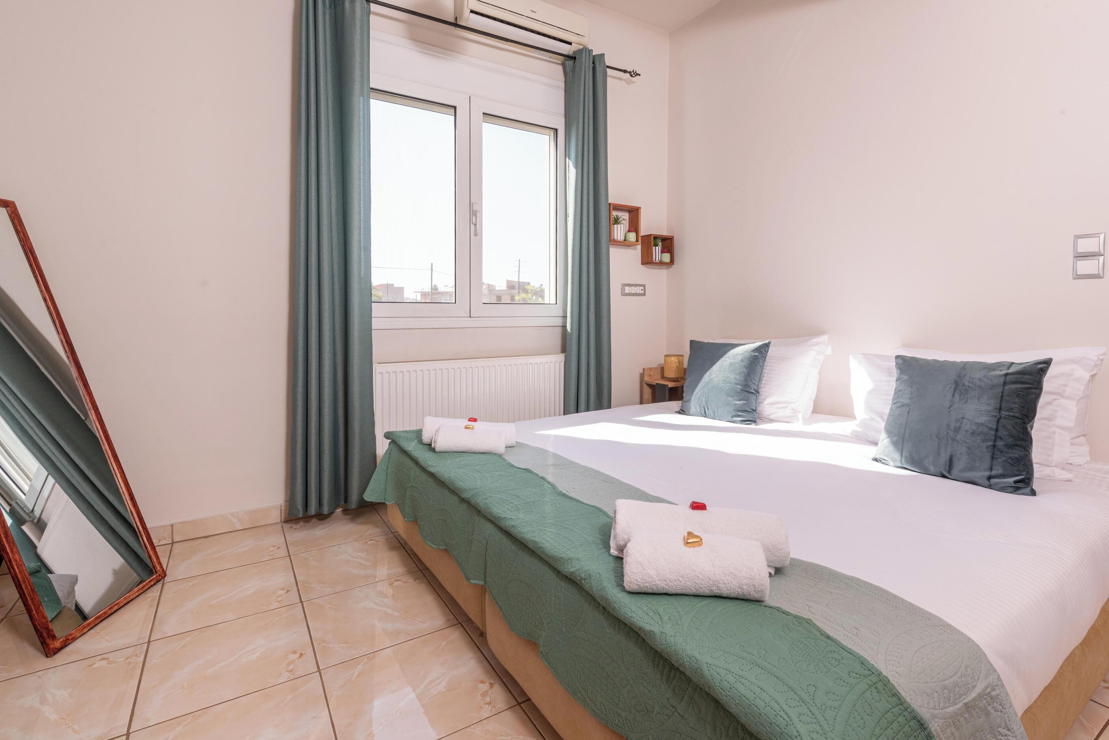 Una habitación de hotel con cama, ventana con cortinas, mesita de noche y espejo.