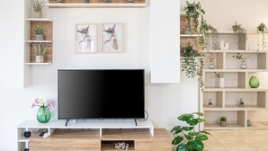 A modern living room with a flat-screen TV, wooden shelves with plants, and framed artwork on the wall. - Lumina Apartment with Shared Pool (Perivolia)