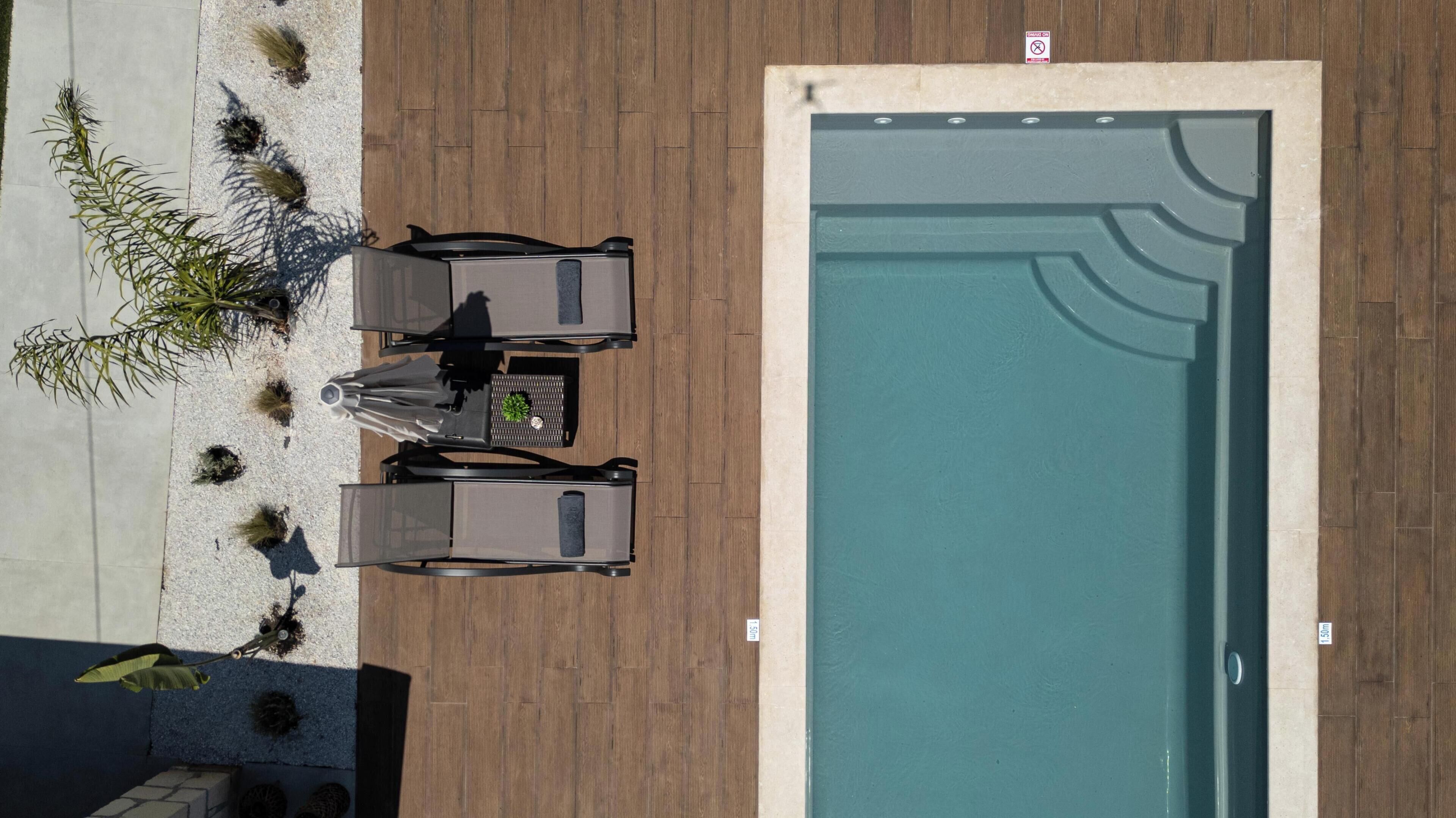 Vista aérea de una zona de piscina con un deck de madera, una mesa con sillas y un pequeño jardín con plantas.