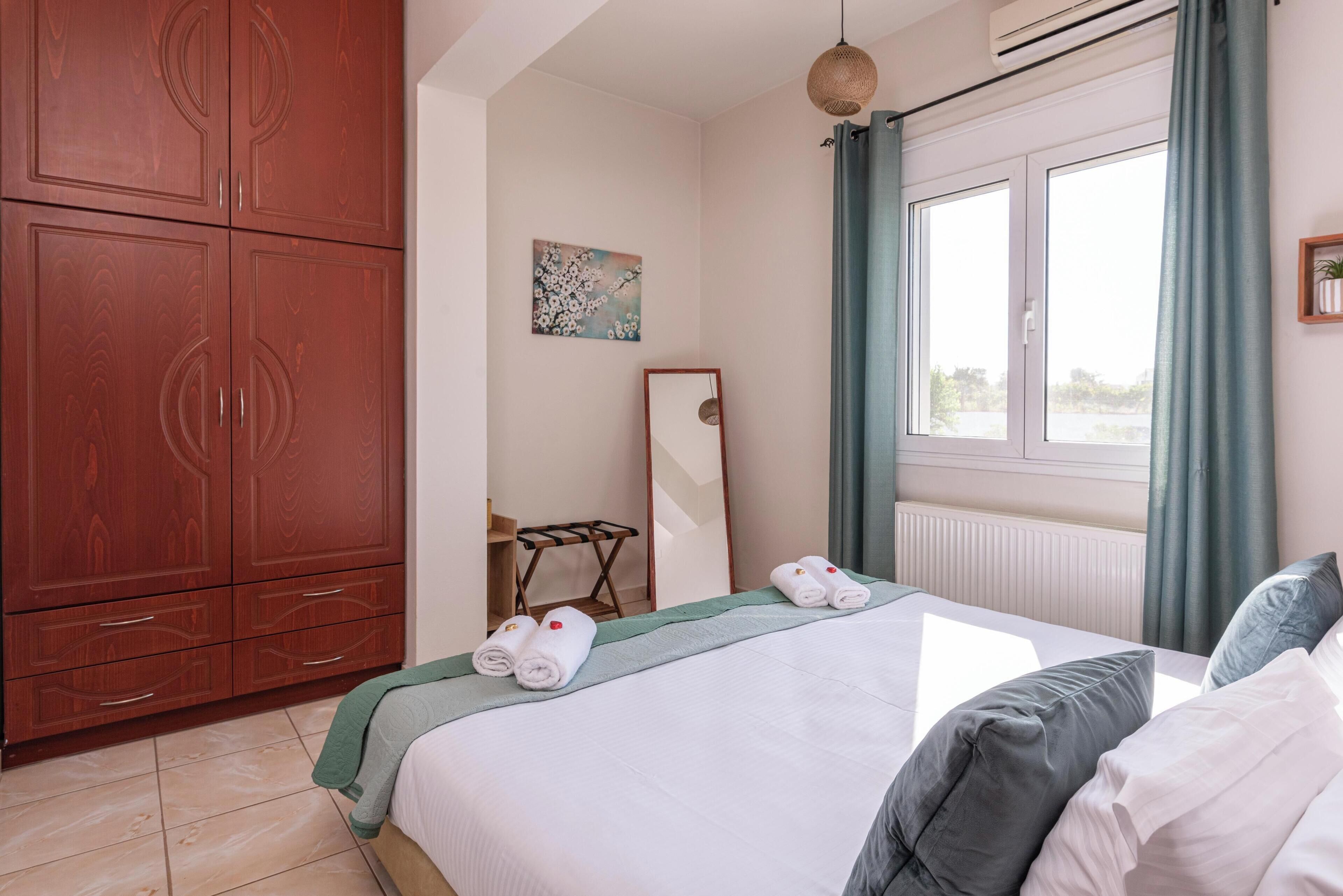 A hotel room with a bed, a wardrobe, a mirror, and a window with curtains.