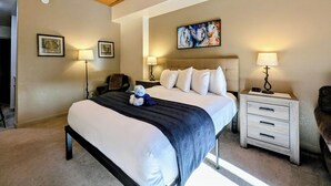 Un dormitorio con una cama, dos mesitas de noche con lámparas, un cabecero y un cuadro en la pared.