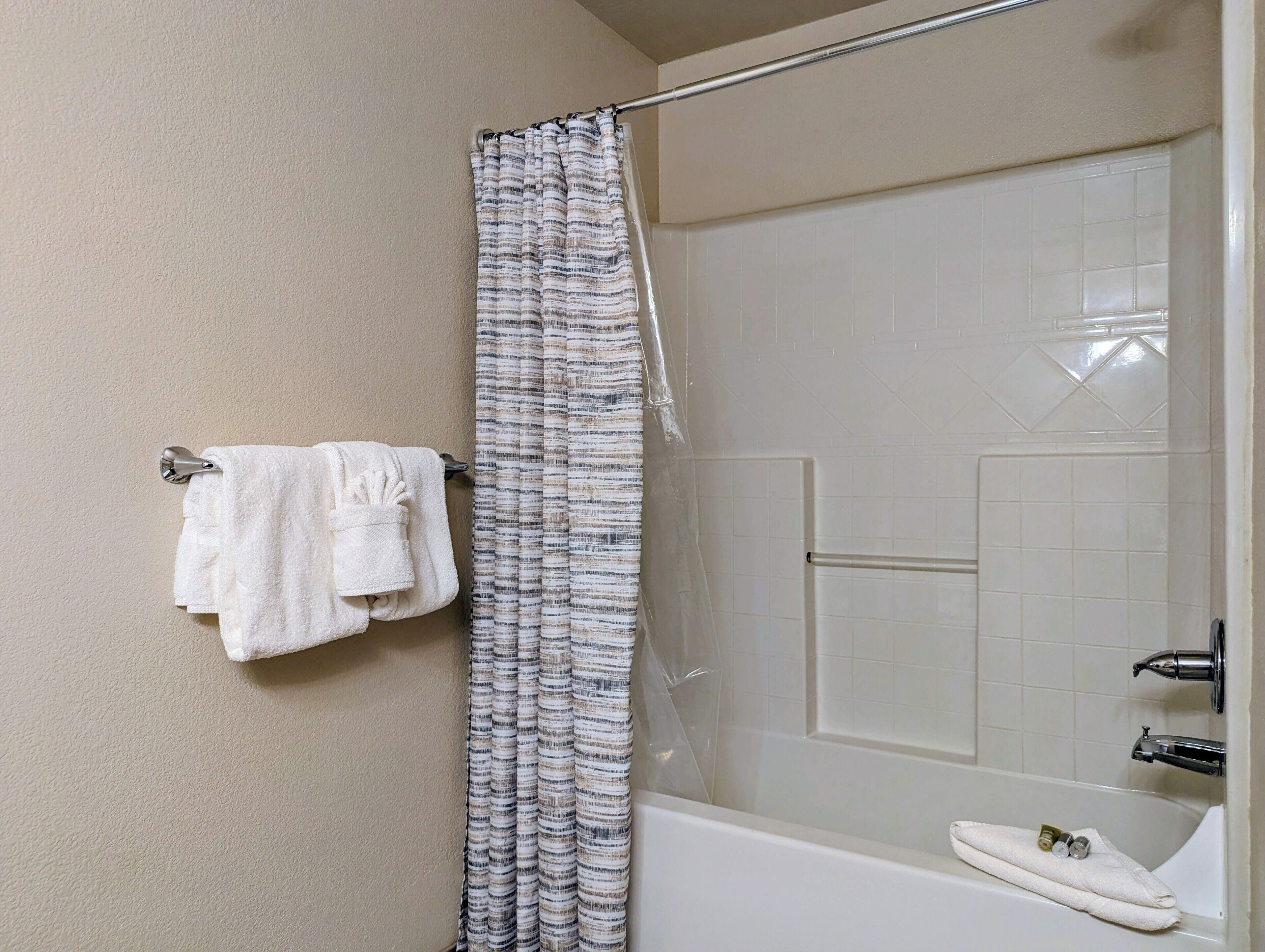 A bathroom with a shower curtain, a towel rack with towels, and a bathtub.