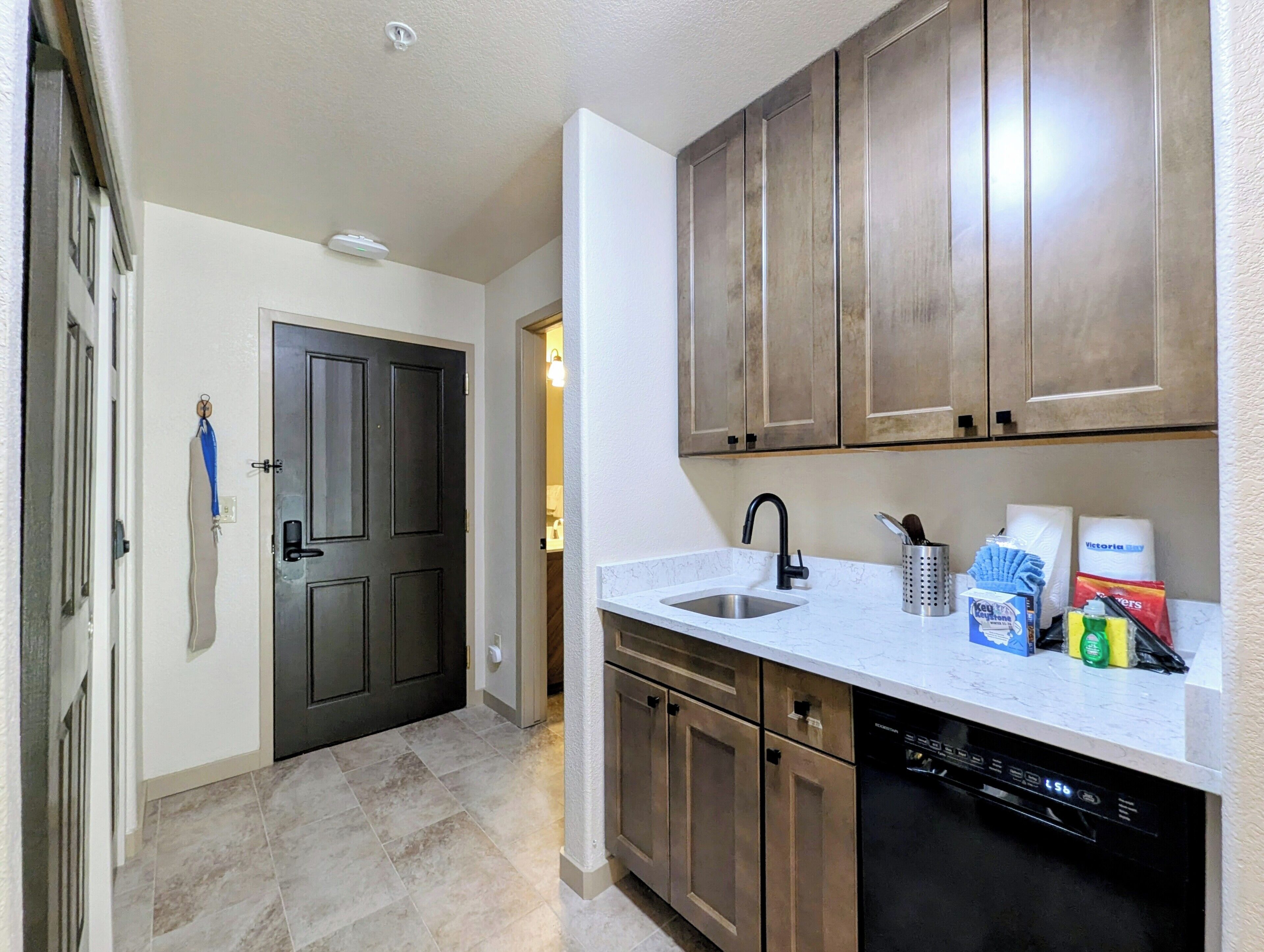 A kitchen with wooden cabinets, a white countertop, a black dishwasher, and a sink.