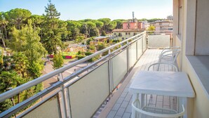 A balcony with a white table and chairs, overlooking a park with trees and buildings. - Central Flat Very Close to the Beach in Eraclea (Eraclea)