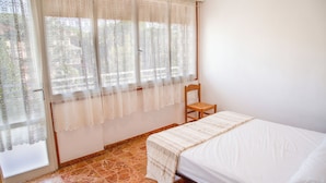 A bedroom with a bed, a chair, and a window with lace curtains. - Central Flat Very Close to the Beach in Eraclea (Eraclea)