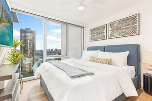 Ein modernes Schlafzimmer mit einem großen Bett, Blick auf die Stadt und einem Balkon mit einer Pflanze.