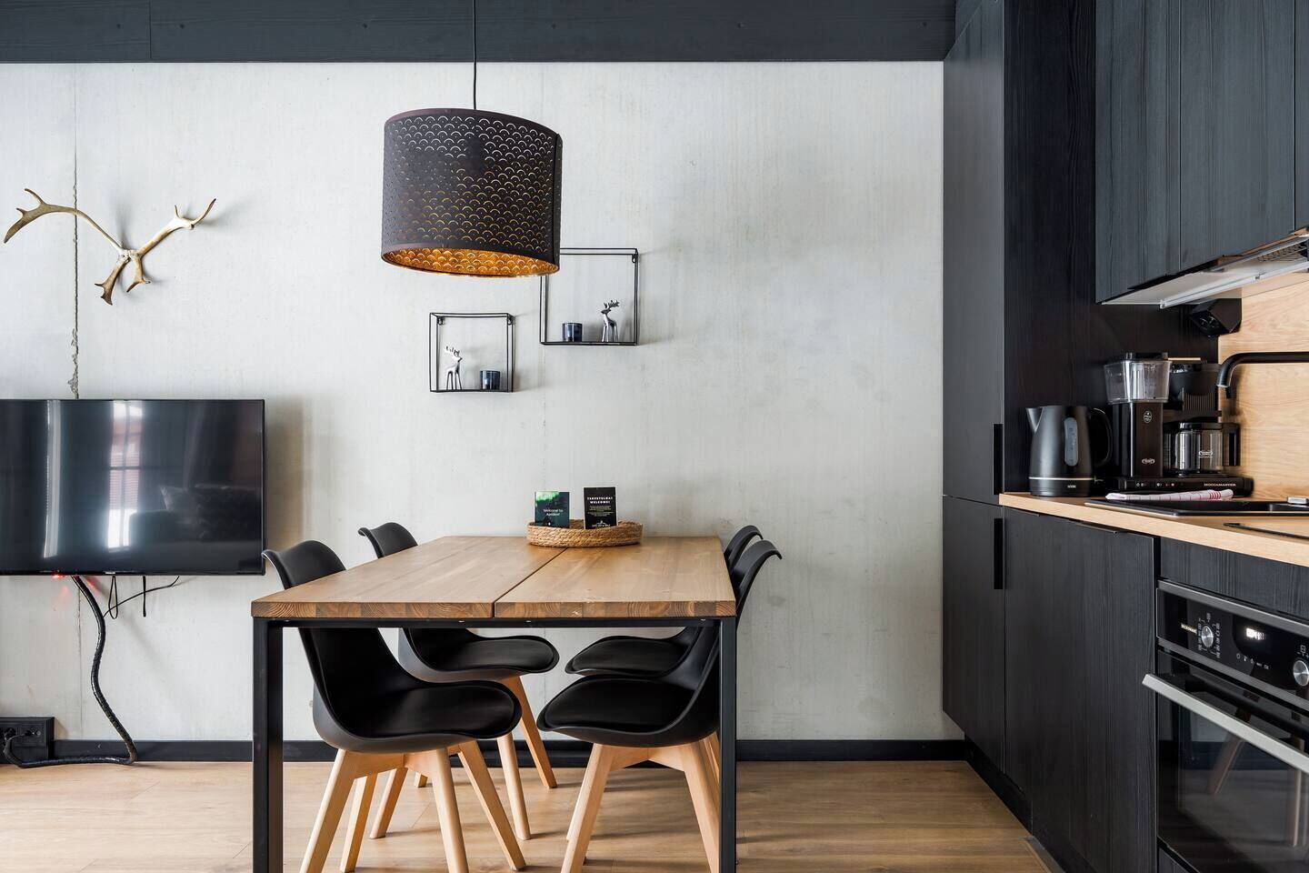 Een moderne keuken met een houten eettafel, zwarte stoelen, een hanglamp en een inbouwoven.