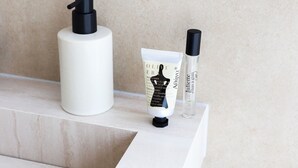 A bathroom vanity with a white marble countertop, a white soap dispenser, a tube of lotion, and a bottle of perfume. - Dam Residence's Classic Suite (Zaandam)