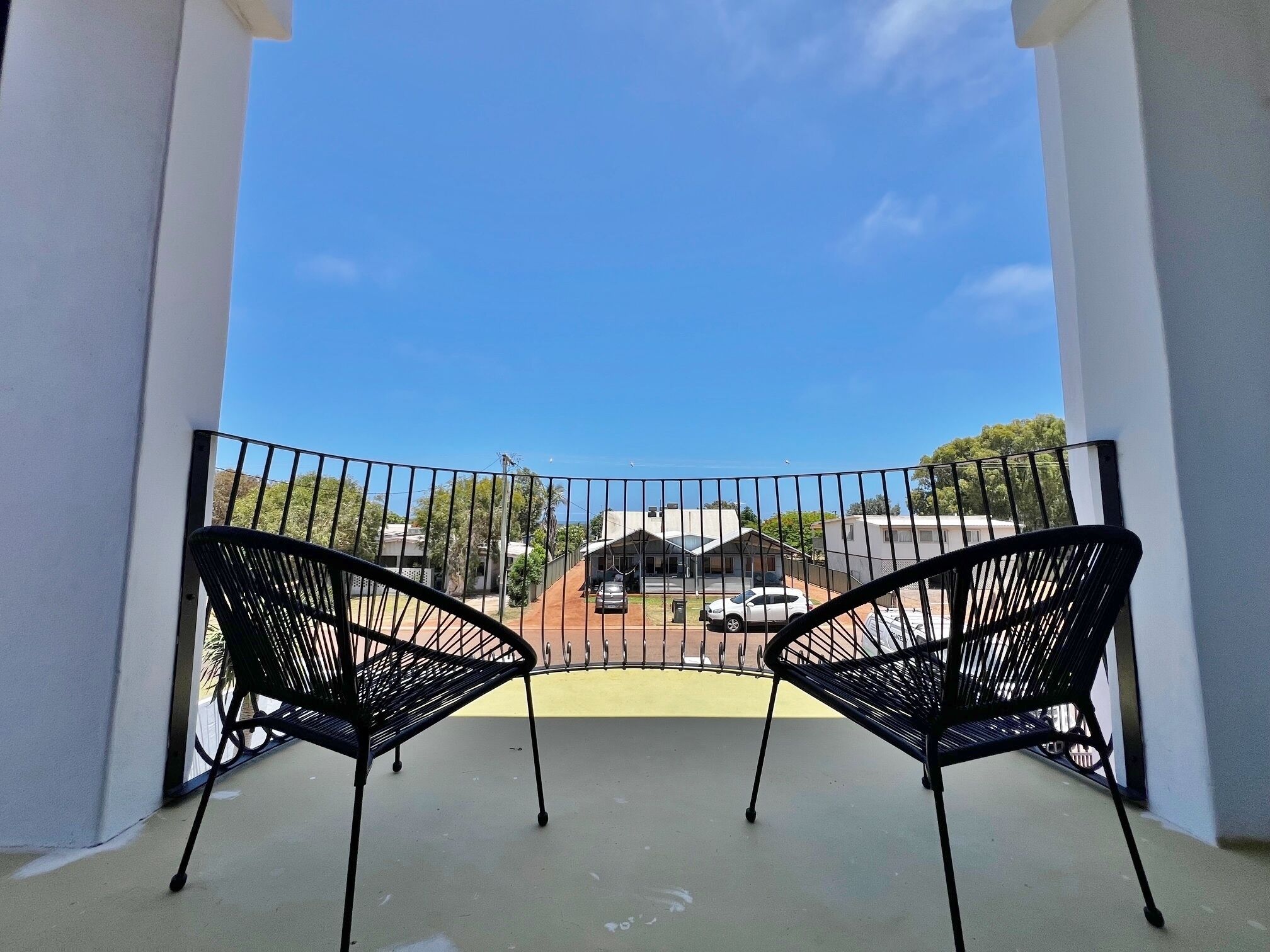 Een balkon met twee zwarte metalen stoelen, gericht op een omheind gebied met gebouwen op de achtergrond.