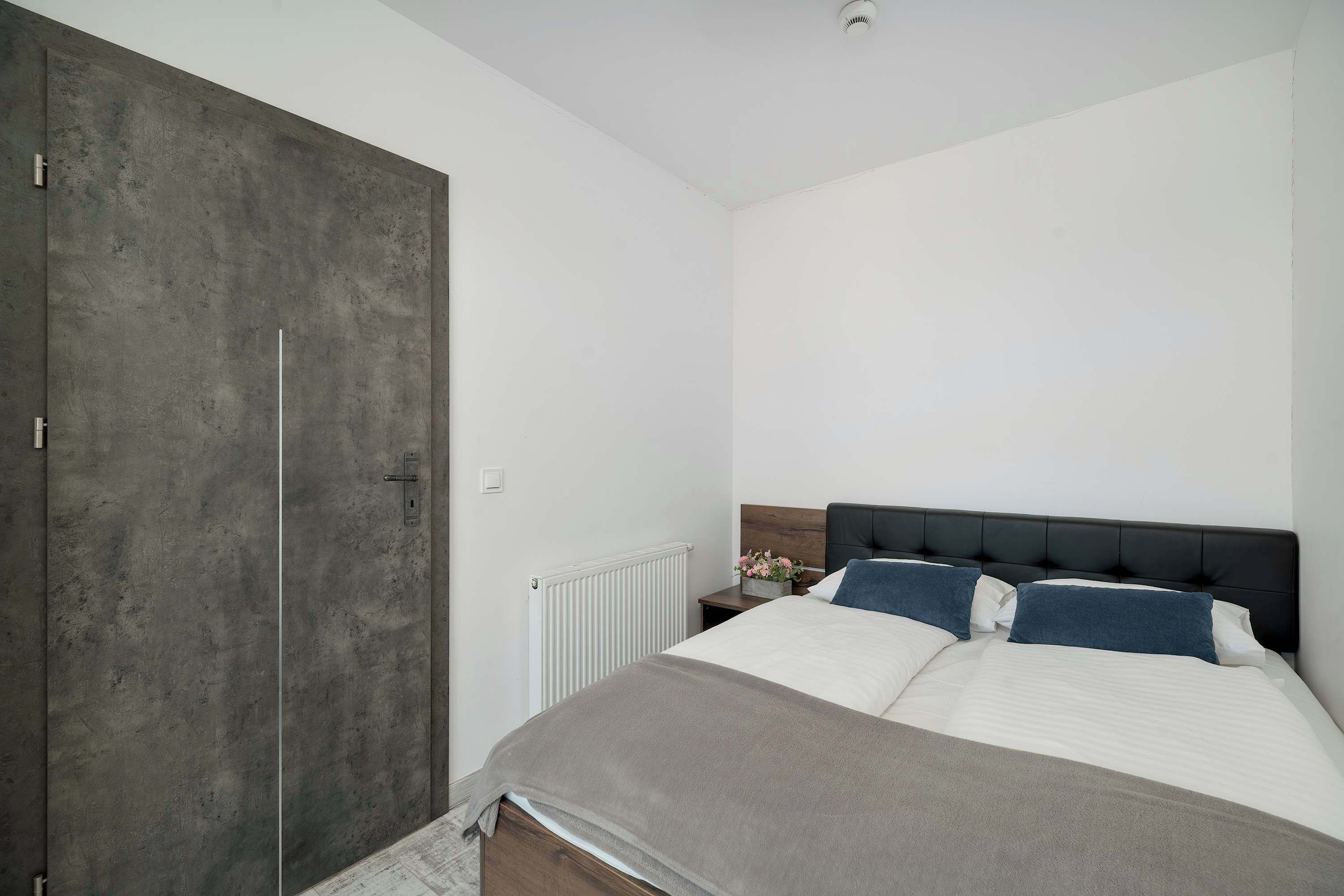 A bedroom with a large wardrobe, a bed with white and blue bedding, and a white radiator.