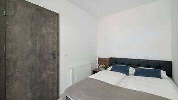 A bedroom with a large wardrobe, a bed with white and blue bedding, and a white radiator.