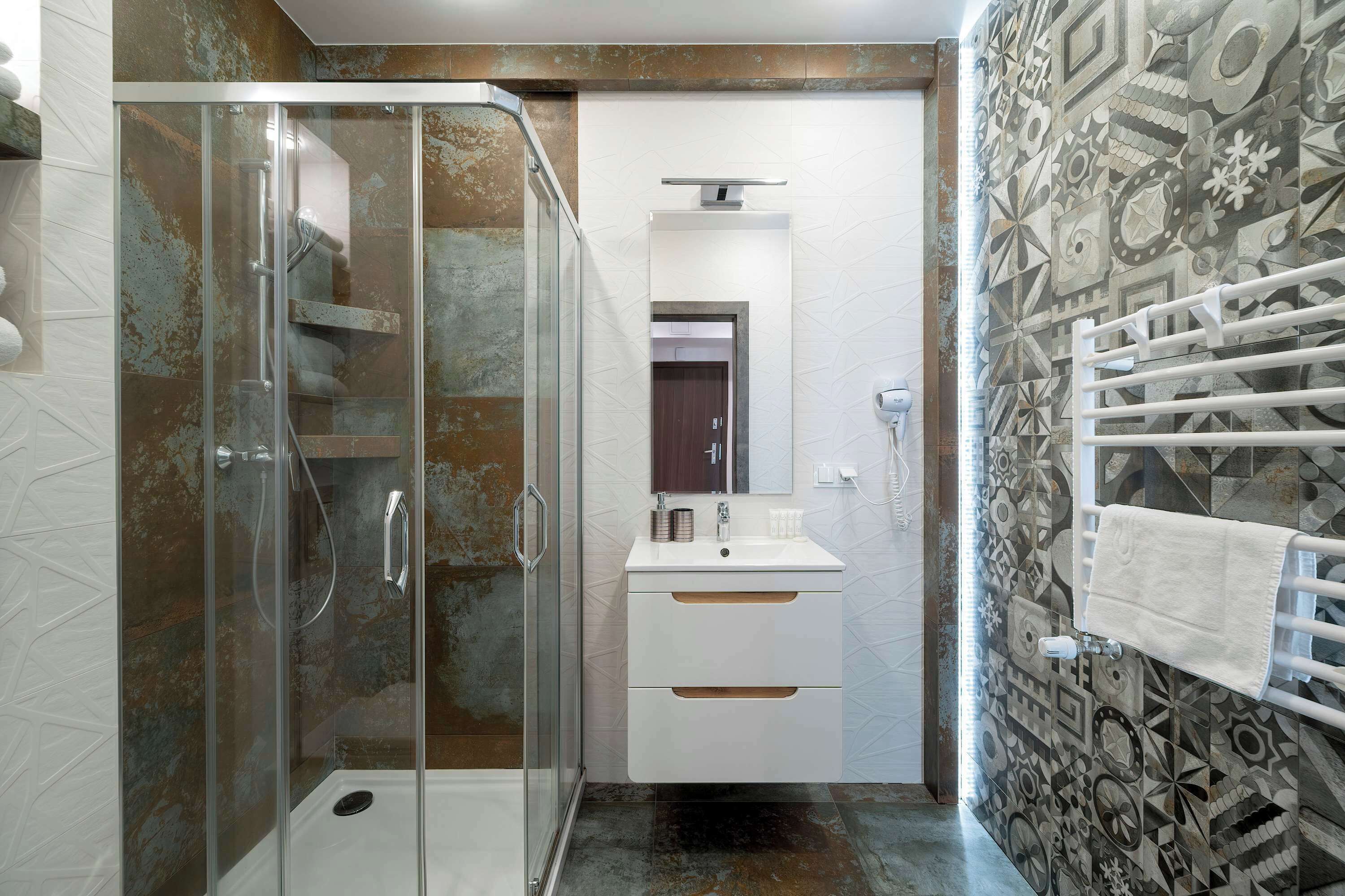 A modern bathroom with a glass-enclosed shower, a white sink with a mirror, and patterned tiles on the walls.