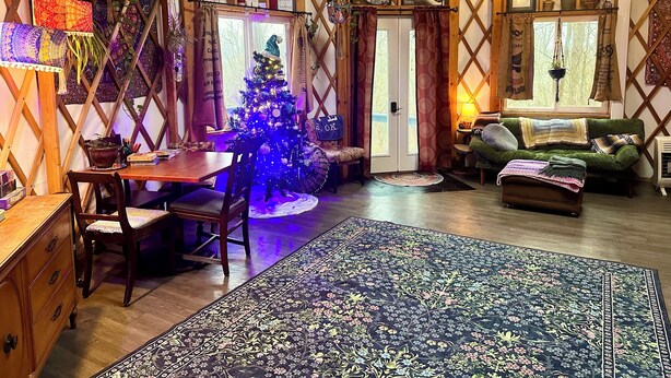 A cozy, rustic interior with a wooden ceiling, a Christmas tree, a dining table with chairs, a sofa, and a patterned rug. - Boho Yurt Stay ~ Cozy & Unique ~ Massage Chair (Athens)