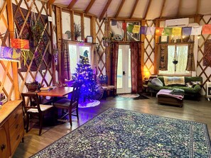 A cozy, rustic interior with a wooden ceiling, a Christmas tree, a dining table with chairs, a sofa, and a patterned rug. - Boho Yurt Stay ~ Cozy & Unique ~ Massage Chair (Athens)