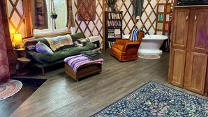 A cozy room with a green sofa, a brown armchair, a bookshelf, a white bathtub, and a wooden cabinet. - Boho Yurt Stay ~ Cozy & Unique ~ Massage Chair (Athens)