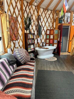 A cozy room with a wooden lattice wall, a white bathtub, a bookshelf, and a patterned sofa.