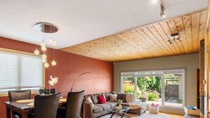 A cozy living room with a dining area, wooden ceiling, and large windows. - Urban Oasis - Heated Pool/Hot Tub - Steam Shower - Pets (Edmonton)