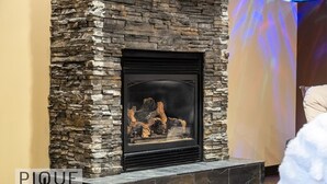 A stone fireplace with a black frame, set in a tiled base. - Urban Oasis - Heated Pool/Hot Tub - Steam Shower - Pets (Edmonton)