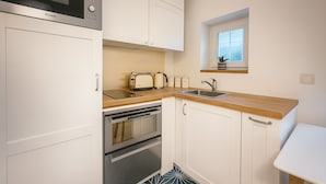 A compact kitchen with white cabinets, a microwave, a toaster, a sink, and a small window above the sink. - Charmant 1 Chambre à Grenelle (Paris)