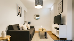A modern living room with a dark sofa, a small wooden table, a TV on a white stand, and a mirror on the wall. - Charmant 1 Chambre à Grenelle (Paris)