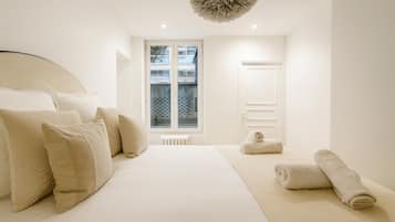 A minimalist bedroom with a large bed, a radiator, and a window with a view of buildings.