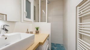 A modern bathroom with a white sink, a mirror, a shower, and a blue tiled floor. - Charmant 1 Chambre à Grenelle (Paris)