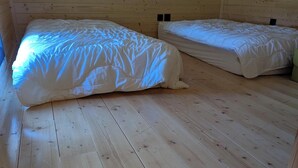 Une petite chambre mansardée, chaleureuse et accueillante, avec des murs et des planchers en bois, deux lits et un plafond en pente.