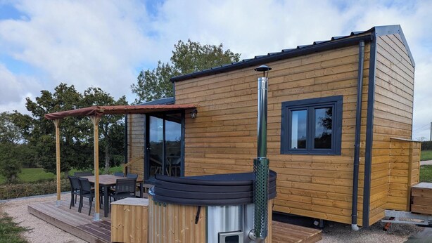 Une cabane en bois dotée d’un bain à remous, d’un espace détente avec mobilier de jardin et d’une pergola.