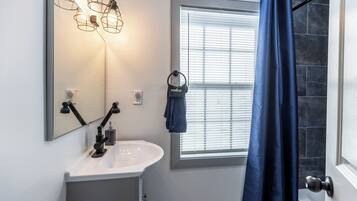 Un baño con lavamanos blanco, un espejo y una ventana con persianas.