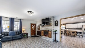Een woonkamer met een open haard, een bank en een keuken met barstoelen.