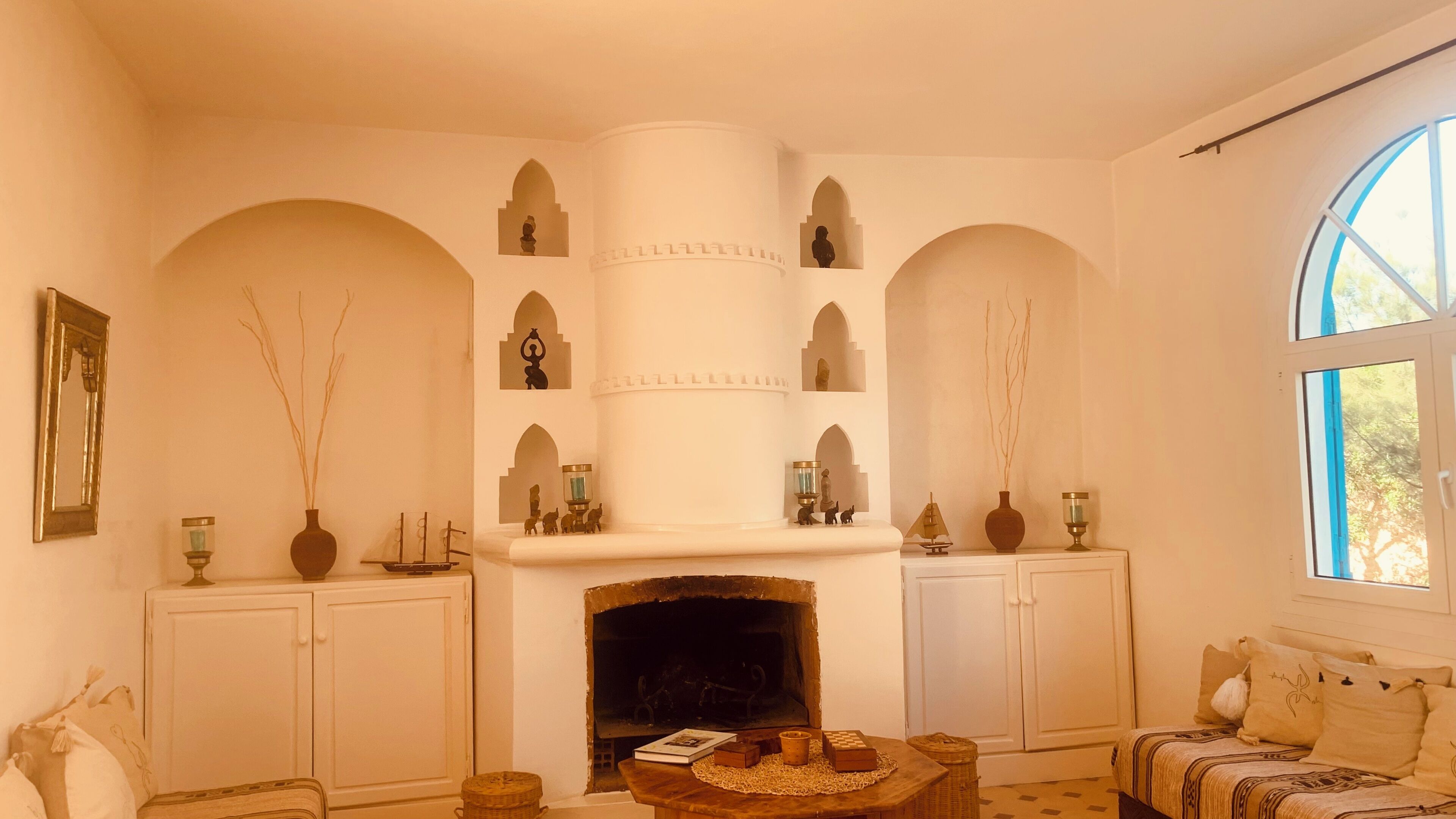 Un salon chaleureux avec une cheminée, des murs blancs et des portes en arc de cercle.