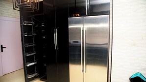 A stainless steel refrigerator with a digital display, a black cabinet with shelves, and a tiled floor. - Luxurious Duplex in Oredo, Benin City - Perfect for Families and Groups (Benin City)