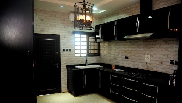 A modern kitchen with black cabinetry, a white countertop, and a patterned backsplash. - Luxurious Duplex in Oredo, Benin City - Perfect for Families and Groups (Benin City)