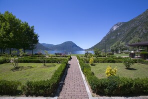 Ein gepflasterter Weg führt zu einem See, im Hintergrund sind Berge zu sehen.