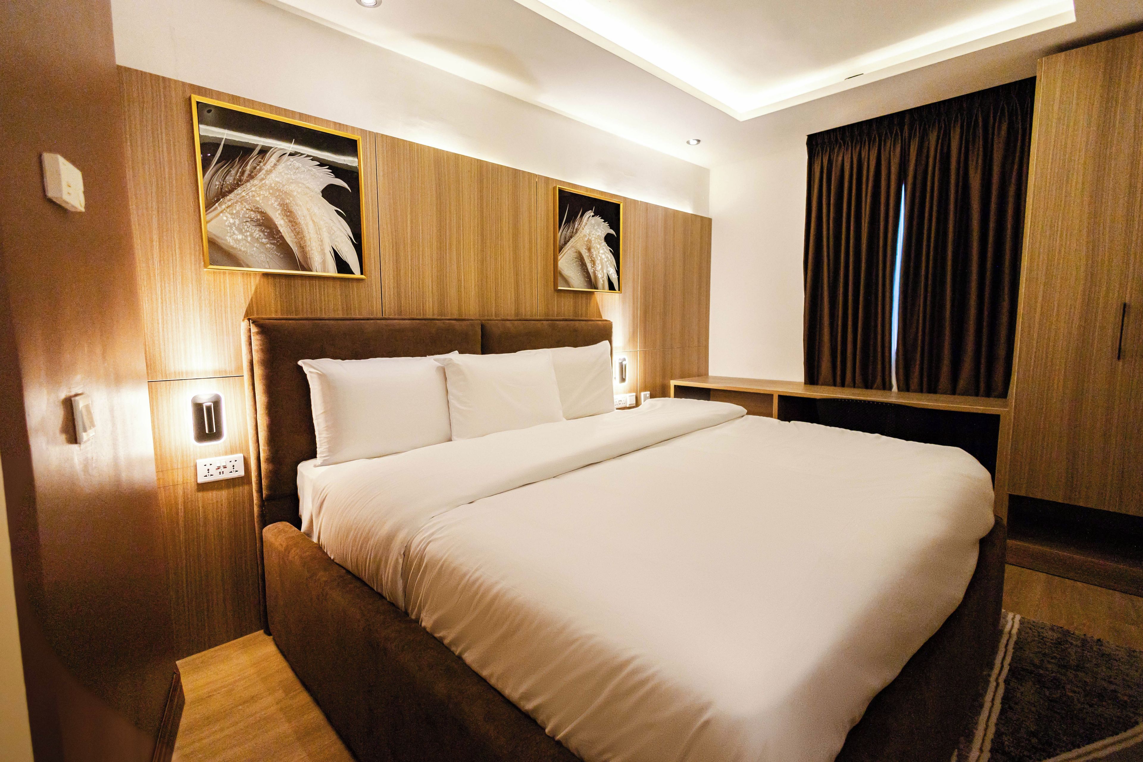 Habitación de hotel con una cama grande, cabecera de madera, dos luces fijadas a la pared y una cortina oscura.