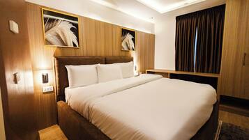 Habitación de hotel con una cama grande, cabecera de madera, dos luces fijadas a la pared y una cortina oscura.